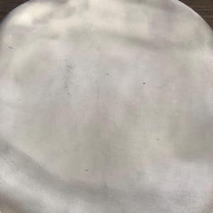 May include: A close-up shot of a silver-colored, oval-shaped object. The surface has a slightly textured appearance with subtle variations in tone, creating a soft, diffused effect. The object appears to be made of metal.