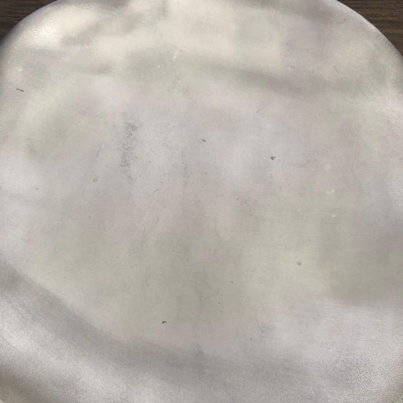 May include: A close-up shot of a silver-colored, oval-shaped object. The surface has a slightly textured appearance with subtle variations in tone, creating a soft, diffused effect. The object appears to be made of metal.