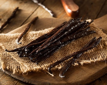 May include: A close-up of a bunch of dried vanilla beans on a burlap surface. The beans are dark brown and have a glossy sheen. They are arranged in a pile on the burlap, which is a natural, rough-textured fabric.