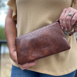 May include: A brown leather clutch purse with a silver zipper and a wrist strap.