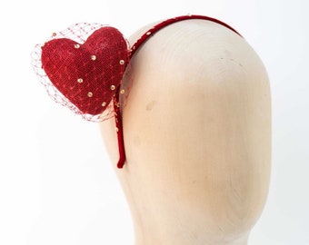 May include: Red velvet heart headband with gold glitter and a red tulle veil. The headband is on a mannequin head.