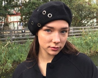 May include: A black beret with silver eyelets. The beret is worn by a person with long brown hair.