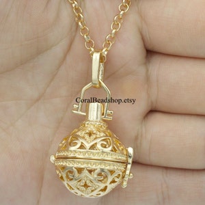 May include: Gold-tone necklace featuring a filigree cage pendant. The pendant has a hinged opening and a delicate chain.