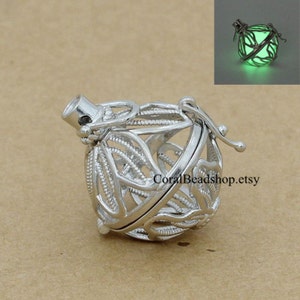 May include: A silver-toned metal cage pendant featuring an intricate filigree design. The spherical charm opens to reveal a glowing green orb, as shown in the inset image. The text CoralBeadshop.etsy is visible on the surface of the pendant.