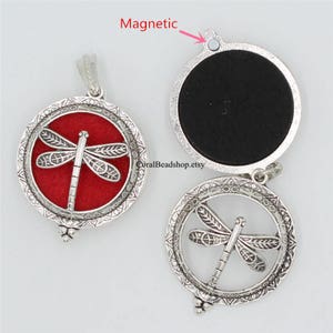 May include: Two round silver-toned metal pendants featuring a dragonfly motif. One pendant is closed with a red felt insert, while the other is open, revealing a black interior and a small magnetic closure point labeled with the text Magnetic.
