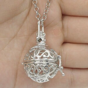 May include: Silver necklace with a delicate, ornate, openwork cage pendant. The cage is round and has a small, decorative latch.