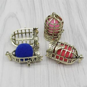 May include: Ornate, antique gold-colored cage pendants, some open, some closed, each containing a colorful sphere. One cage holds a blue sphere, another a pink sphere, and a third a red sphere. The cages have decorative scrollwork.