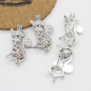 May include: Four silver cat charm pendants with open bellies to hold a pearl or other small object. The charms are in various poses, including sitting, standing, and walking. The charms are a delicate and intricate design.
