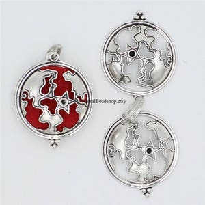 May include: Three circular silver-toned metal pendants featuring a cutout map design with a central star. One pendant has a red enamel inlay, while the other two are openwork silver. Each piece includes a small bail at the top for attachment.