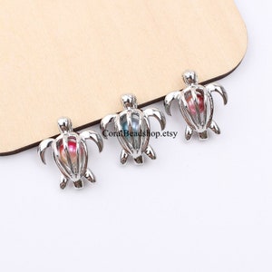 Op de afbeelding: Drie zilveren schildpadbedels, elk met een parel. De parels zijn in verschillende kleuren: roze, blauw en groen.