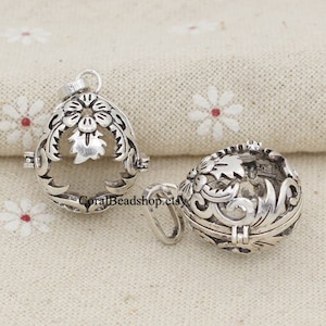 May include: Two silver-toned metal charm pendants with intricate floral designs. The pendants are open and have a hinged lid. The pendants are approximately 1 inch in diameter.