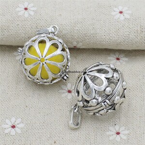 Può includere: Due ciondoli in argento con un design a forma di fiore. Un ciondolo ha un fiore giallo all'interno. Entrambi i ciondoli hanno un piccolo anello nella parte superiore per essere attaccati a una catena.