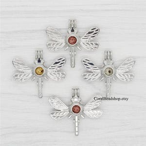 May include: Four silver dragonfly charm pendants with clear glass orbs. Each orb contains a different colored stone. The charms are perfect for adding a touch of nature to jewelry.