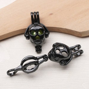 May include: Two black skull-shaped charm pendants with a green pearl inside. The pendants have a loop at the top for attaching to a necklace or bracelet. The pendants are connected by a black metal chain.