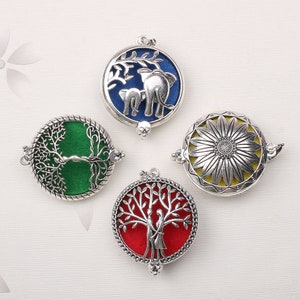Puede incluir: Cuatro colgantes de plata con diferentes diseños. Los colgantes están abiertos y muestran un árbol verde, un árbol rojo con dos personas, un elefante azul y un girasol amarillo.