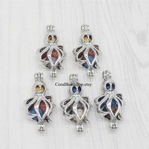 Puede incluir: Cinco colgantes de plata con forma de pulpo con una esfera de vidrio transparente en su interior. Cada esfera contiene cuentas de lava de colores. Los colgantes son perfectos para añadir un toque caprichoso a collares, pulseras o llaveros.