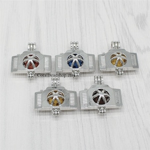 May include: Five silver charm pendants with a cage design. Each cage contains a small, round, colorful orb. The orbs are red, blue, yellow, brown, and purple.