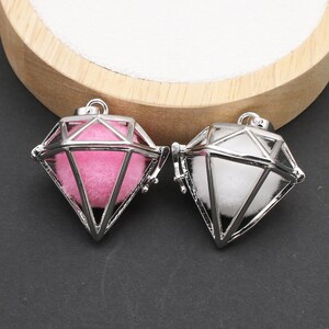 May include: Two silver diamond-shaped cage pendants with a white and pink fluffy ball inside. The pendants are open on one side and have a loop at the top for hanging.