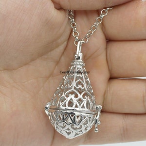 Puede incluir: Un collar con colgante plateado con un diseño de jaula en forma de lágrima. La jaula presenta intrincados recortes en forma de corazón. El collar cuelga de una delicada cadena, creando un accesorio elegante. El colgante mide unos 3 cm.