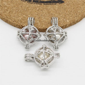 May include: Three silver-toned metal cage pendants, each featuring a spherical design with a hinged opening. Inside each cage is a single round bead in shades of pink, white, or cream. The text CoralBeadshop.etsy is visible on the pendants.