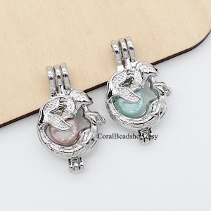 May include: Two silver mermaid charm pendants with a pearl inside. The mermaid is curled around the pearl. One pearl is pink and the other is light blue.