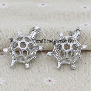 May include: Two silver turtle shaped pearl cages. The cages are open and have a delicate, intricate design.