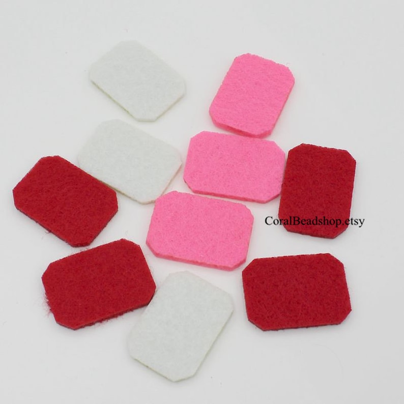 May include: A collection of ten rectangular felt pieces with clipped corners in shades of white, pink, and red. The felt shapes are arranged in a scattered pattern. The text CoralBeadshop.etsy is visible on the right side of the image.