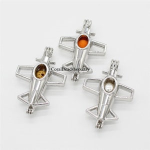May include: Three silver airplane charm pendants with open tops. The charms are designed to hold small items, such as pearls or beads. The charms are shown against a white background.