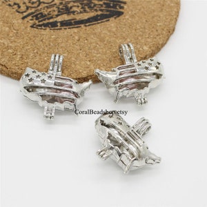 May include: Three silver charm pendants shaped like the outline of the United States with an American flag design. The pendants are open and appear to be for holding a pearl or other small object.