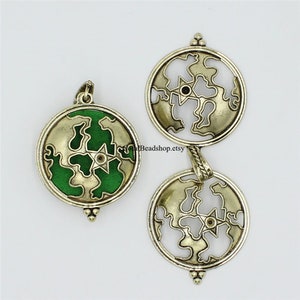 May include: Three circular silver-toned metal pendants featuring a cutout world map design with a central star. One pendant includes a green enamel inlay within the landmasses. Each piece has a small decorative bead at the bottom and a bail at the top.