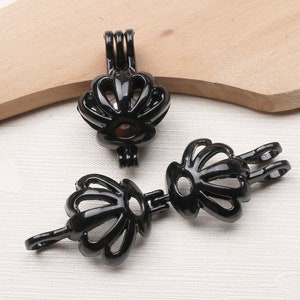 Peut inclure: Deux pendentifs en métal noir en forme de coquille de mer avec une petite ouverture. Le pendentif de gauche a une boucle en haut et une chaîne qui le relie au pendentif de droite. Le pendentif de droite a une boucle sur le côté.