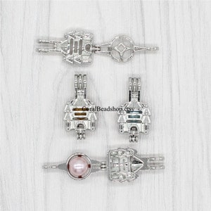 May include: Silver charm with a castle design. The charm is open and can be used to hold a pearl or other small object. The charm is shown with a pearl inside.