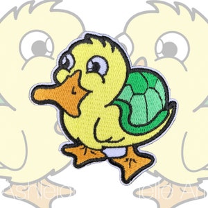 Puede incluir: Un parche bordado con un pato de dibujos animados que lleva una concha de tortuga verde. El pato tiene un gran pico naranja y ojos blancos.