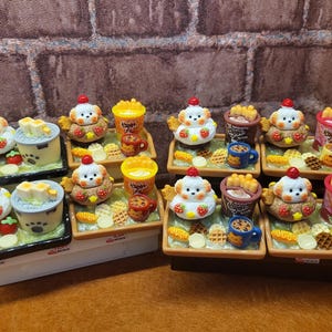 May include: Miniature food sets featuring a dog-shaped character with a cherry on its head, paired with various treats like waffles, fries, and drinks. The sets are arranged on small trays, showcasing a playful and colorful aesthetic.