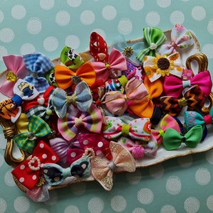 May include: A collection of colorful hair bows in various patterns and sizes, displayed on a decorative, off-white, heart-shaped dish with gold accents. The bows feature polka dots, stripes, and floral designs, with some embellished with rhinestones and pearls.