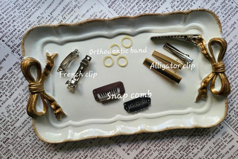 May include: A collection of hair accessories including French clips, alligator clips, snap combs, and orthodontic bands. The items are in silver, gold, and brown tones, arranged on a decorative white tray with gold accents.
