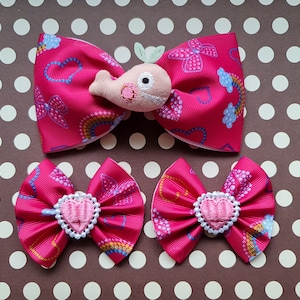 Könnte beinhalten: Drei rosa Haarbänder mit einem weißen Herzdesign. Das größere Band hat eine rosa Wal-Applikation mit einem grünen Blatt oben drauf.