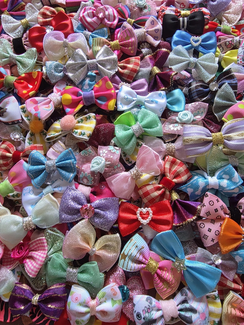 May include: A collection of colorful hair bows in various sizes and designs. The bows feature a variety of colors, including pink, blue, green, and purple, with some adorned with rhinestones and other embellishments. The bows are made of different materials, such as satin and grosgrain.