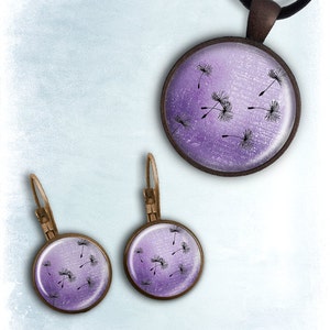 May include: A set of purple and silver jewelry featuring a necklace and earrings with a dandelion design. The necklace has a round pendant with a purple gradient and black dandelion seeds. The earrings are also round with a purple gradient and black dandelion seeds.