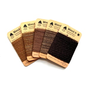 Peut inclure: Cinq bobines de fil brun, beige et noir étiquetées "Mend" et "Mend it" avec le texte "Limited Edition Upcycled Yarn" et "Approx. 10 m 15 m 20 m".