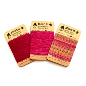 May include: Three spools of limited edition upcycled yarn in shades of pink and orange. The yarn is labeled "Mend it" and includes the fiber content: Alpaca, Angora, Cashmere, Cotton, Lambswool, Mohair, Nylon, Silk, Wool, and Yak.