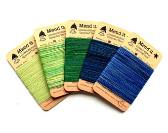 Könnte beinhalten: Fünf Spulen limitierter Upcycling-Garn in verschiedenen Farben. Das Garn besteht aus Alpaka, Lammwolle, Mohair, Nylon und Yak. Jede Spule ist mit "Mend it" beschriftet und hat eine kleine Illustration eines Hutes.