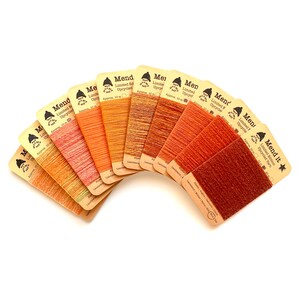 May include: A collection of ten cards of "Mend it" upcycled yarn in various shades of orange and brown. Each card displays a different color of yarn, ranging from light peach to deep rust. The cards are arranged in a fan shape against a white background.