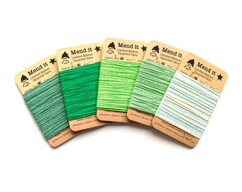 Könnte beinhalten: Fünf Spulen mit grünem, hellgrünem und weißem recyceltem Garn mit der Aufschrift "Mend it Limited Edition Upcycled Yarn" mit einer ungefähren Länge von 15 Metern. Das Garn ist auf braunen Pappspulen mit einem Stern und einer kleinen Illustration einer Person mit Hut verpackt.