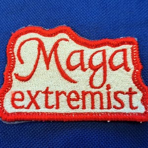 Op de afbeelding: Rode en witte geborduurde patch met de tekst "Maga extremist" in witte letters.