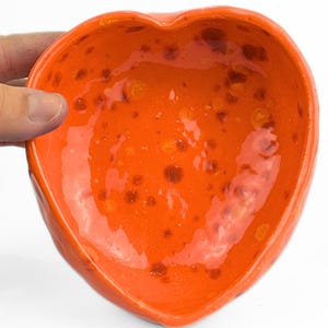 Puede incluir: Tazón de cerámica naranja en forma de corazón con un esmalte moteado.