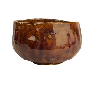 May include: A small, brown ceramic bowl with a textured, uneven surface. The bowl has a glossy finish and a slightly rounded shape.