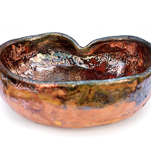 Könnte beinhalten: Eine handgefertigte Keramikschale mit einer einzigartigen, organischen Form. Die Schale hat eine reichhaltige, strukturierte Oberfläche mit einer Mischung aus Kupfer-, Bronze- und Dunkelbrauntönen. Das Innere hat ein glänzendes, irisierendes Finish.
