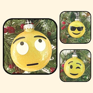 May include: Three yellow Christmas ornaments with different emoji faces. The first ornament has a surprised face with wide eyes. The second ornament has sunglasses and a smile. The third ornament has a winking face.