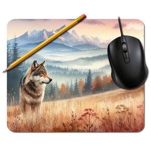 Peut inclure: Tapis de souris rectangulaire avec une peinture à l'aquarelle d'un loup dans un champ avec des montagnes en arrière-plan. Un crayon jaune et une souris d'ordinateur noire sont également présents. La scène a une palette de couleurs chaudes.